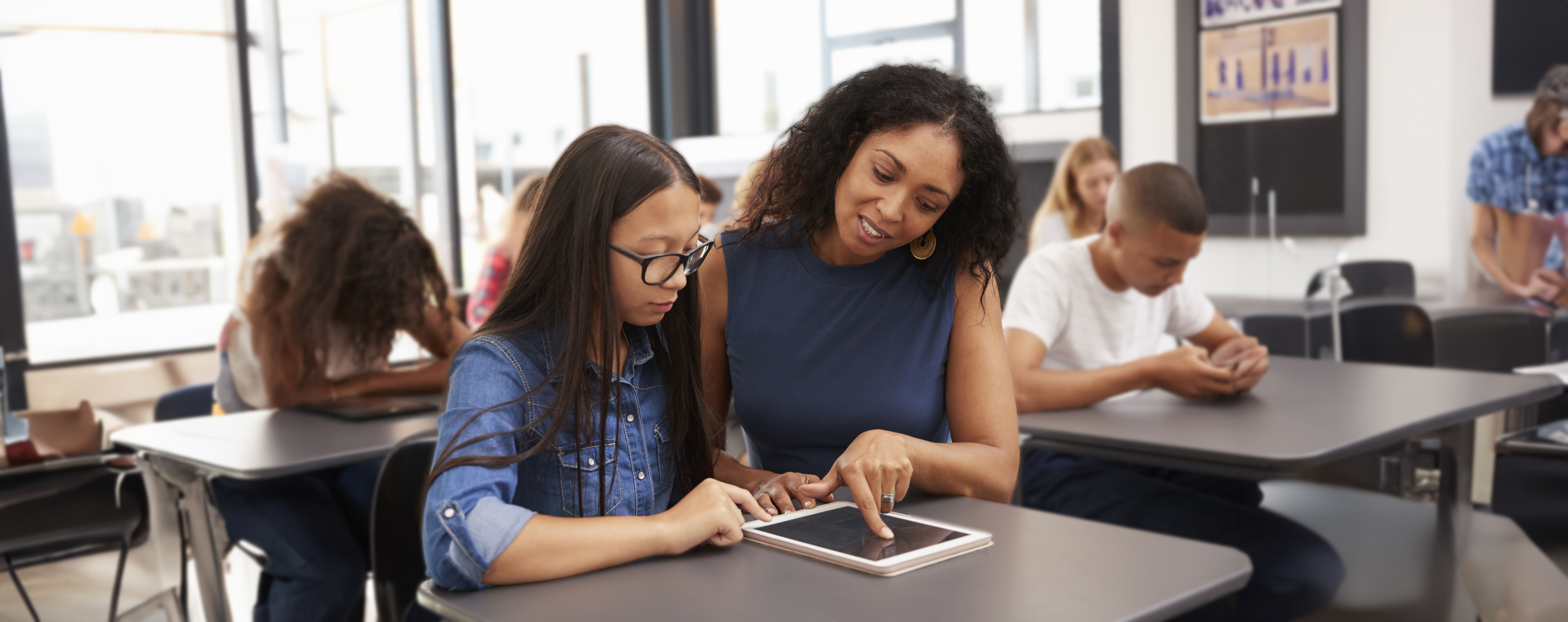 Teacher helping teenage schoolgirl with tablet computer