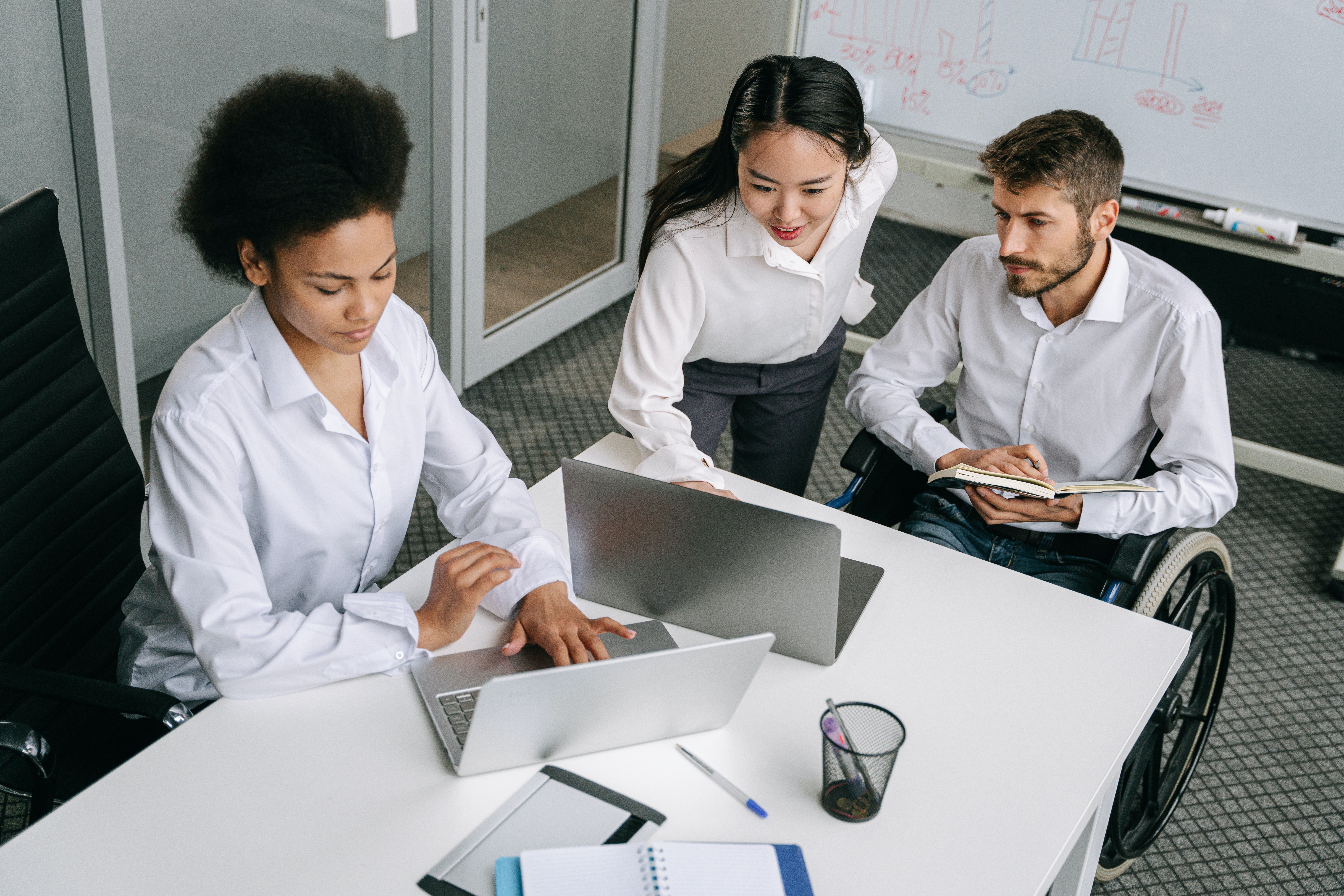 Group of diverse young professionals around a table looking at a laptop