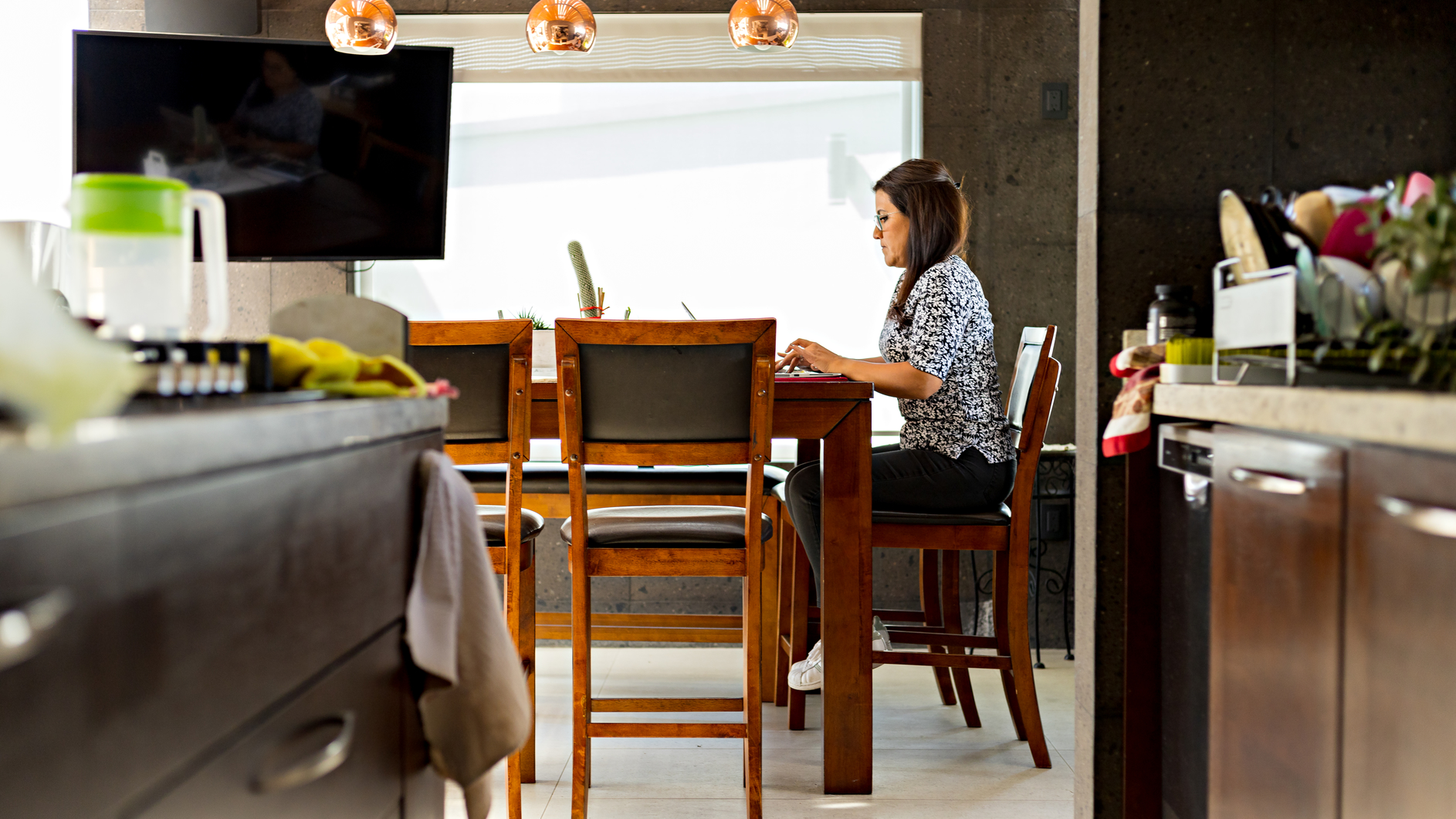 Lady woman typing on her computer sitting at her dining room table. Female person carrying out her work activities remotely from her home.