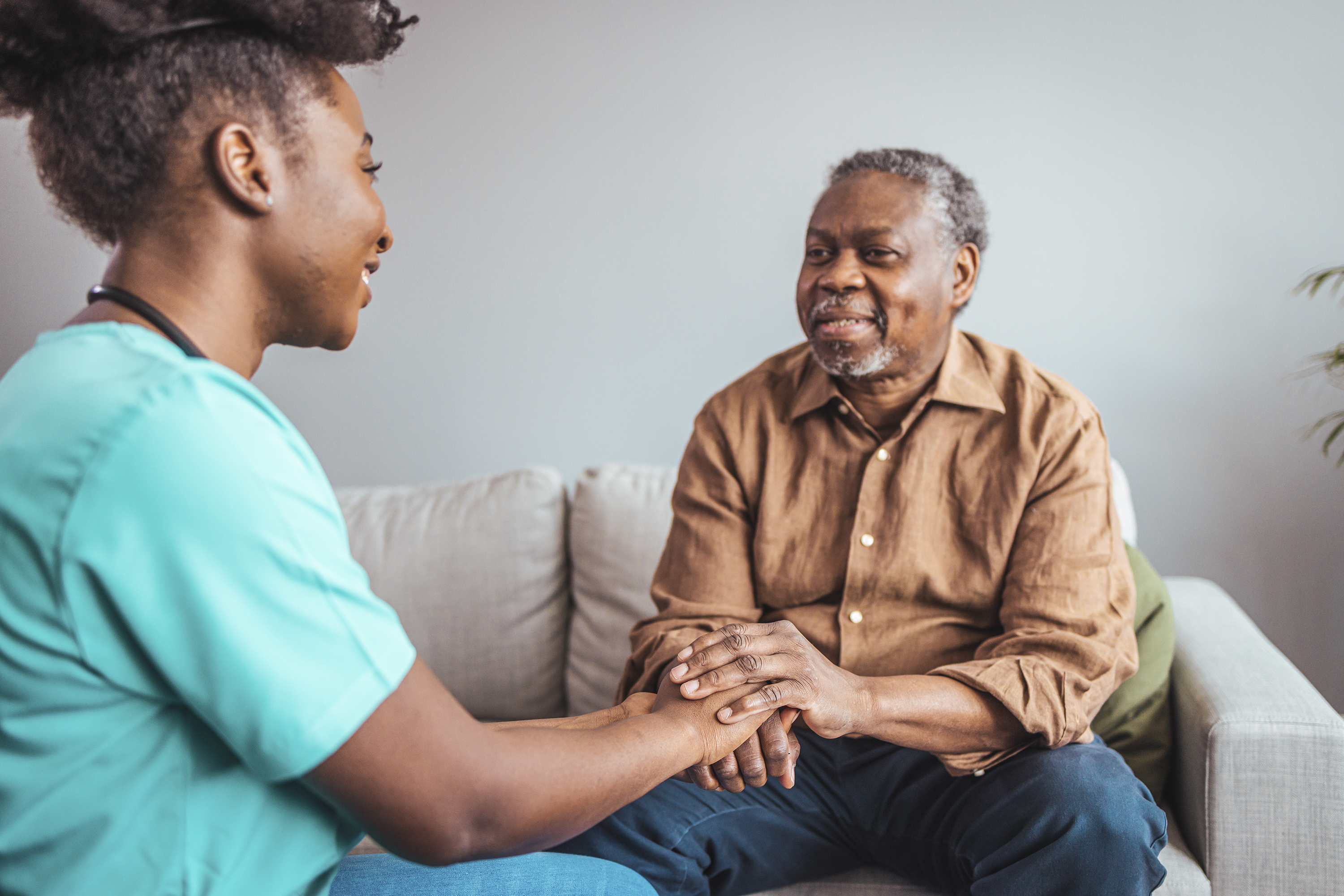 Close-up of health care worker and senior woman holding hands, both African American